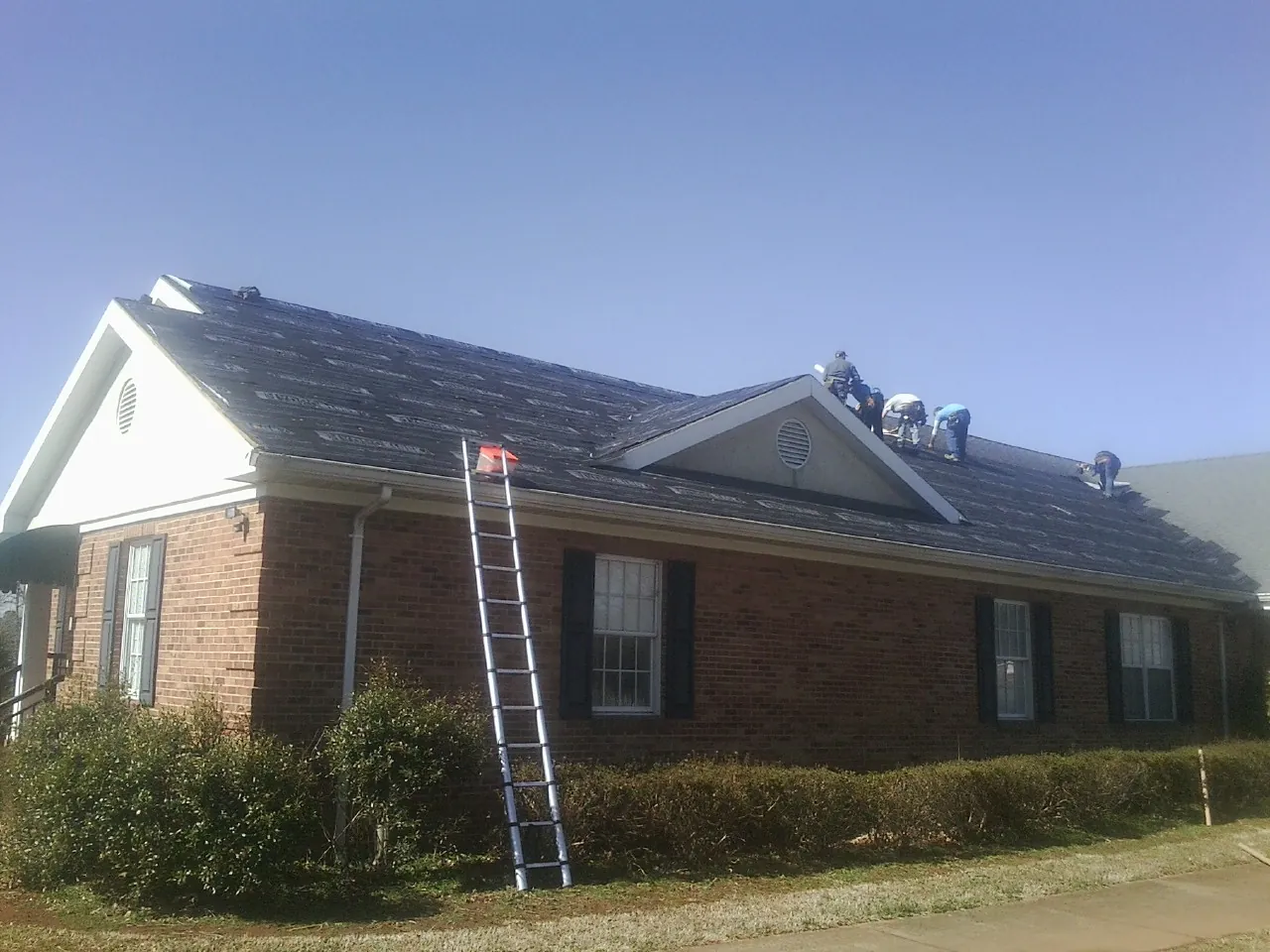 Crew tearing shingles off a brick ranch roof with a ladder set — Metal Roof Repair work by our crew in Germantown